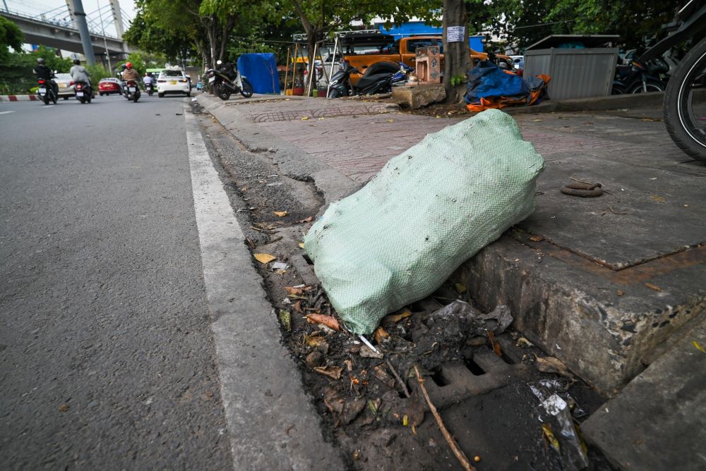 Bao đựng rác chắn nửa miệng cống trên đường Huỳnh Tấn Phát (quận 7) - điểm ngập của TP HCM mỗi khi mưa lớn. “Cứ tối đến khi dọn hàng xong, những người bán hàng rong lại đổ hết rác vào miệng cống. Gặp mưa, rác trôi xuống cống làm tắc, đường ngập. Bà con ở đây đã phản ánh rất nhiều lần rồi nhưng không ăn thua“, ông Lê Đức Dũng, sống ven đường, cho biết.